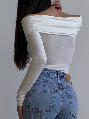 White off-shoulder bodysuit with ruched detail and long sleeves, paired with blue jeans.