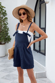 Dark navy linen romper with bow straps and pleated front, styled with a white tank top.