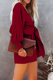 Burgundy tie knot puff sleeve romper with cinched waist and smocked cuffs.