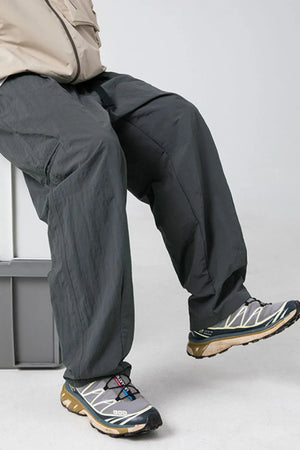 Dark gray technical fabric cargo pants with belt detail and large pockets.