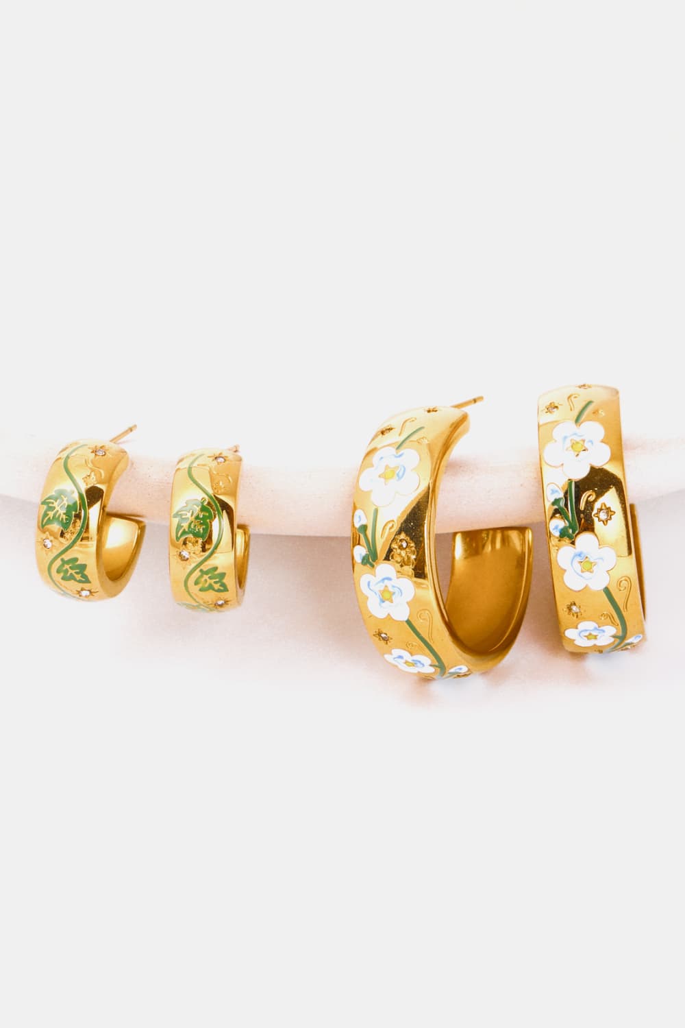 Gold hoop earrings with floral enamel details in white and green.