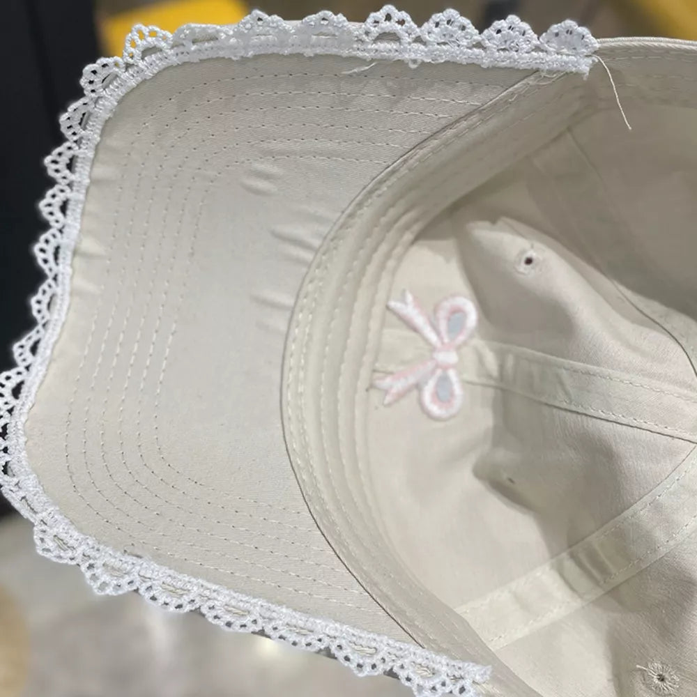Beige baseball cap with embroidered bow detail and white lace trim.