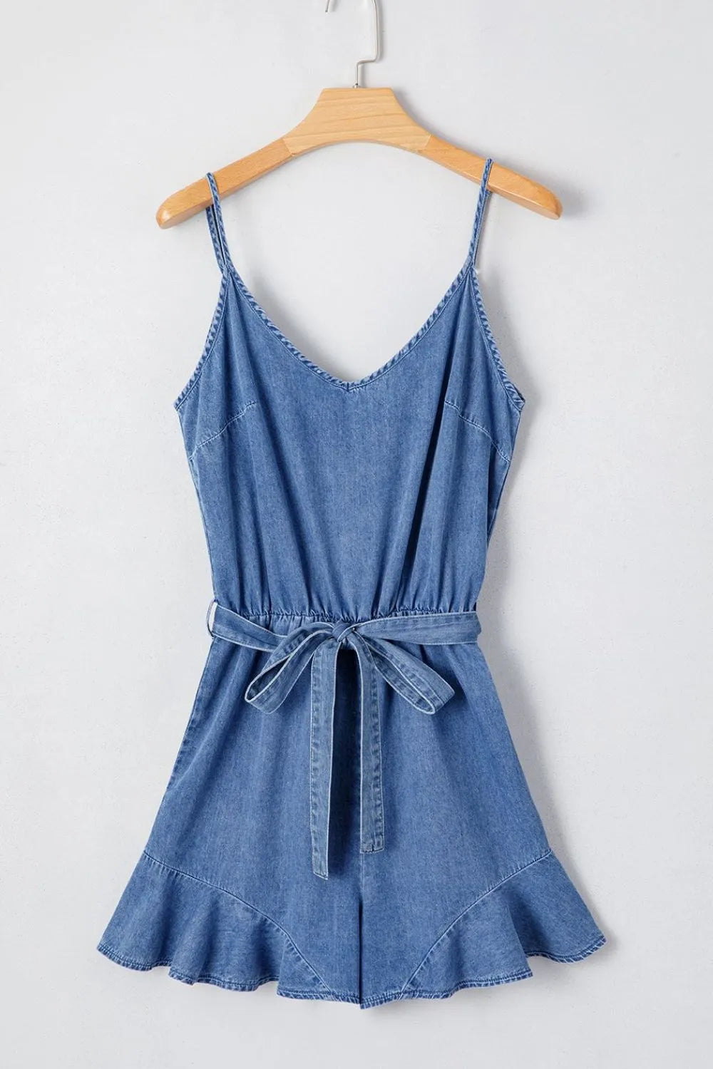 Medium denim romper with spaghetti straps, tie waist, and ruffled hem.
