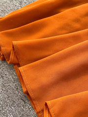 Orange maternity dress detail showing ruffled fabric and white stitching.