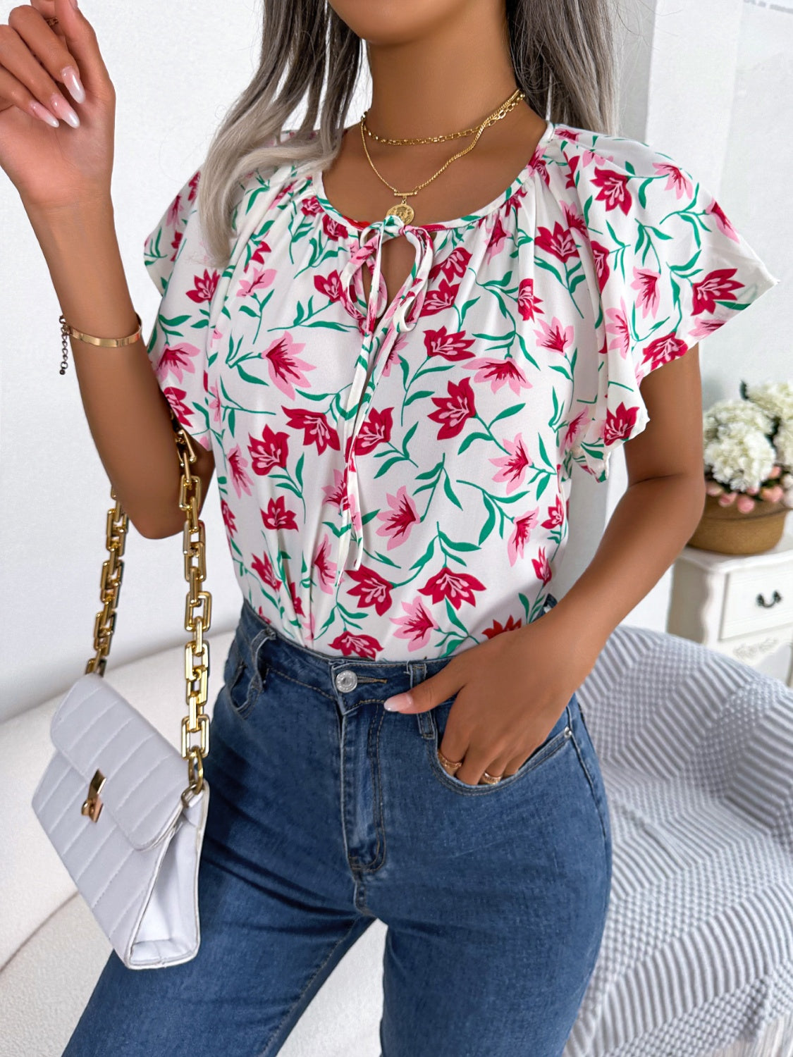 White floral ruffle sleeve tie-neck blouse with pink flowers and green leaves.