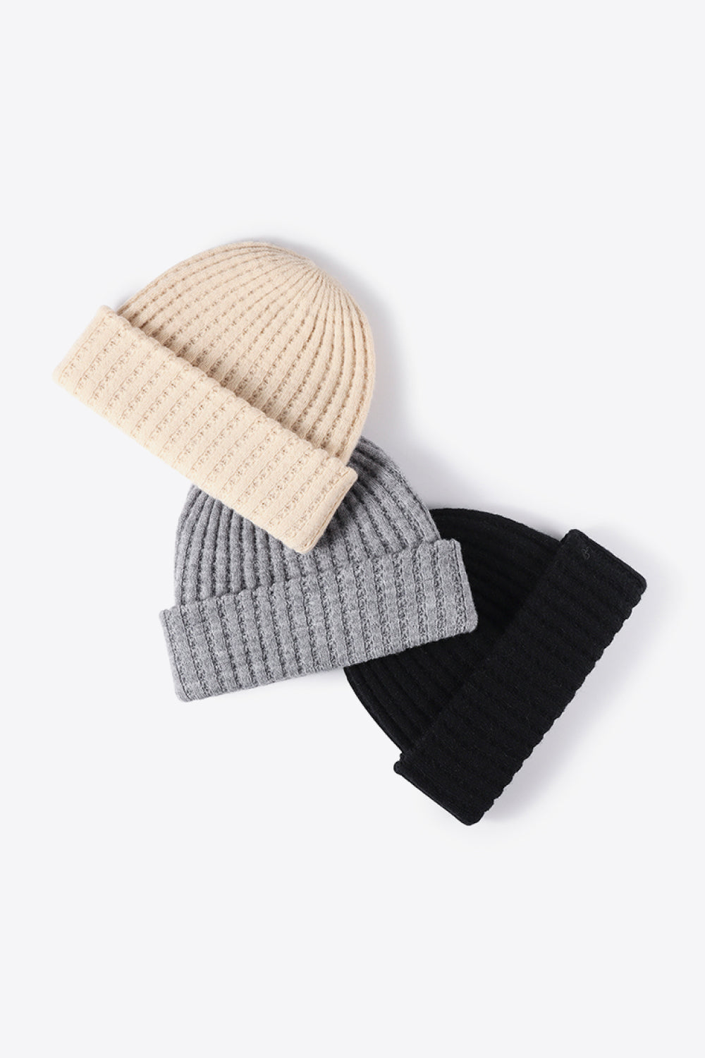 Textured ribbed knit beanies in beige, gray, and black with folded cuffs.