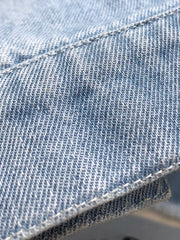 Light wash denim shirtdress detail with visible stitching and raw hem texture.