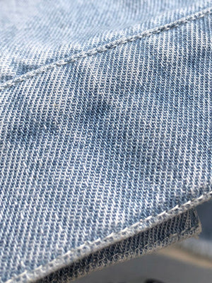 Light wash denim shirtdress detail with visible stitching and raw hem texture.