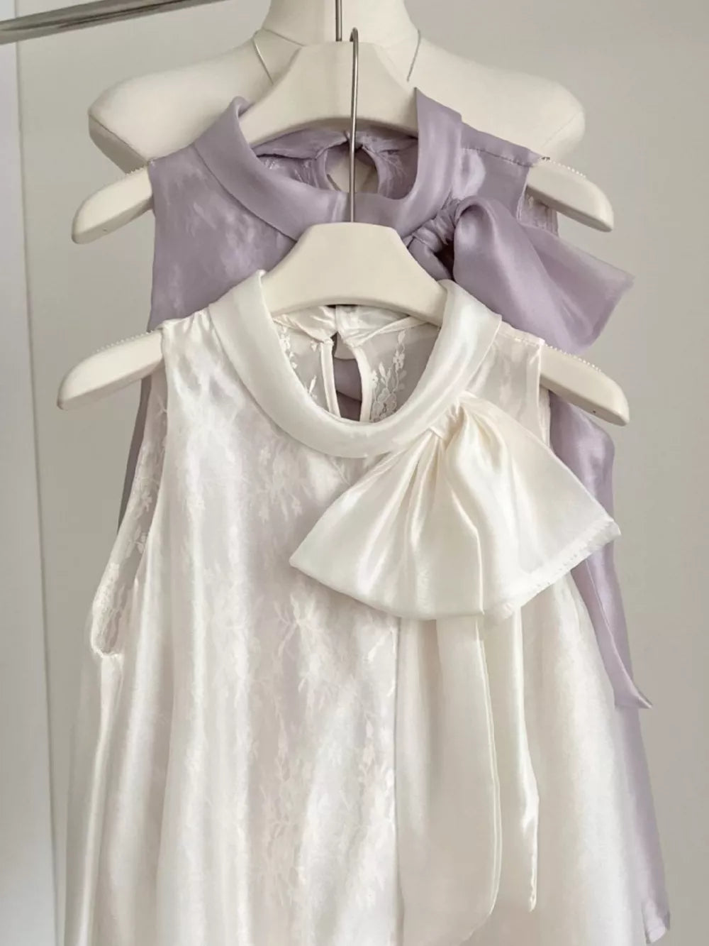 Sleeveless white shirt with lace detail and large satin bow, purple shirt with bow detail.