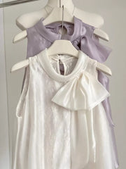 Sleeveless white shirt with lace detail and large satin bow, purple shirt with bow detail.