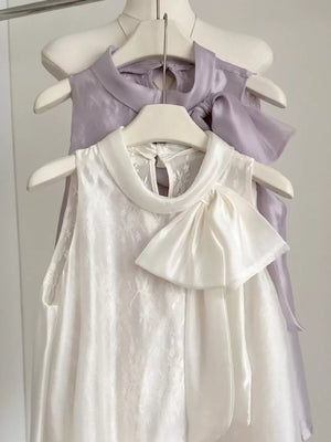 Sleeveless white shirt with lace detail and large satin bow, purple shirt with bow detail.