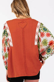 Orange-red blouse with floral patchwork balloon sleeves and heart detail on back.