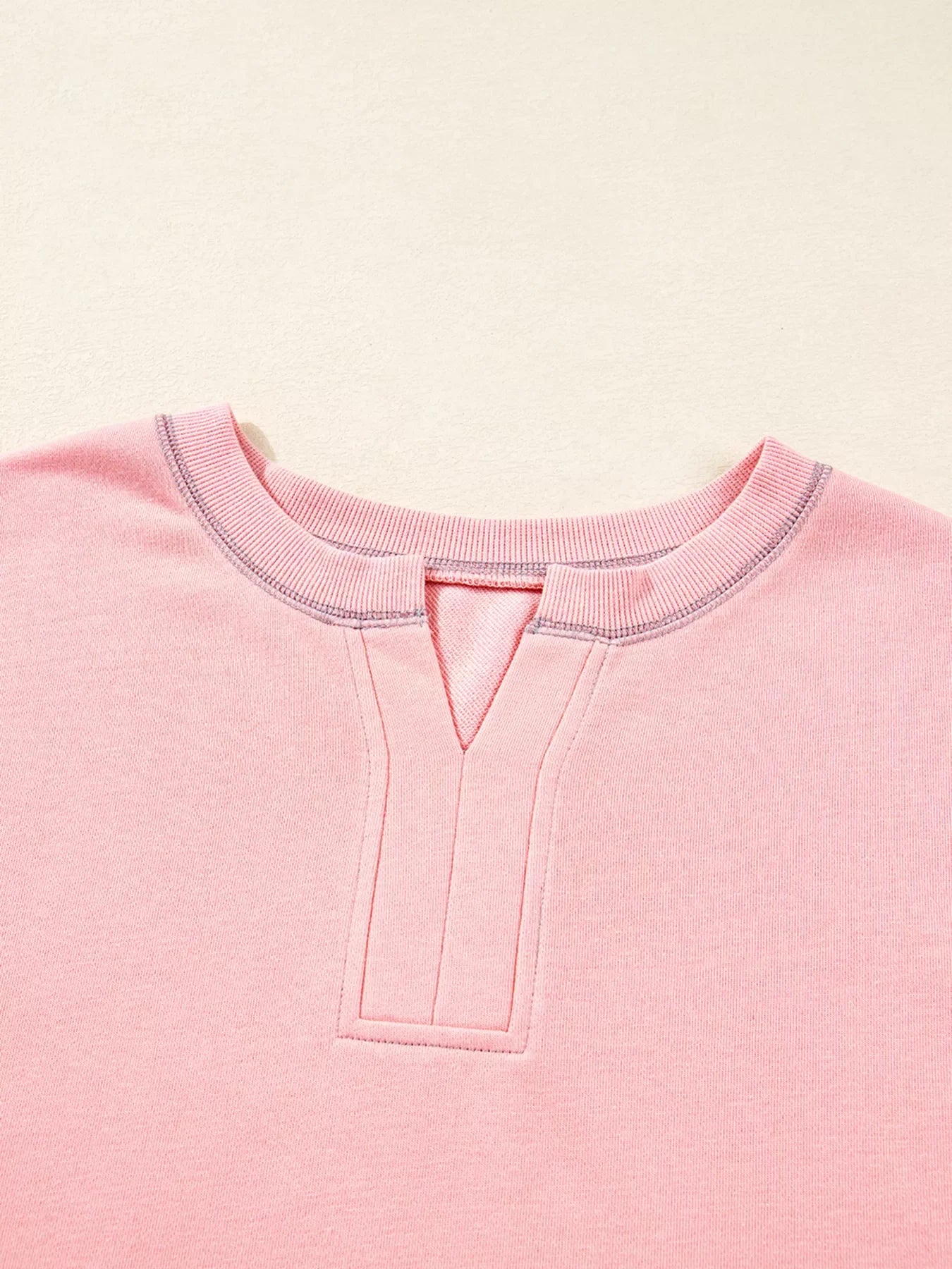 Dusty pink oversized sweatshirt with contrast stitching and a V-neck detail.