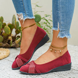 Red slip-on wedge flats with rhinestone-adorned bows and ankle straps.