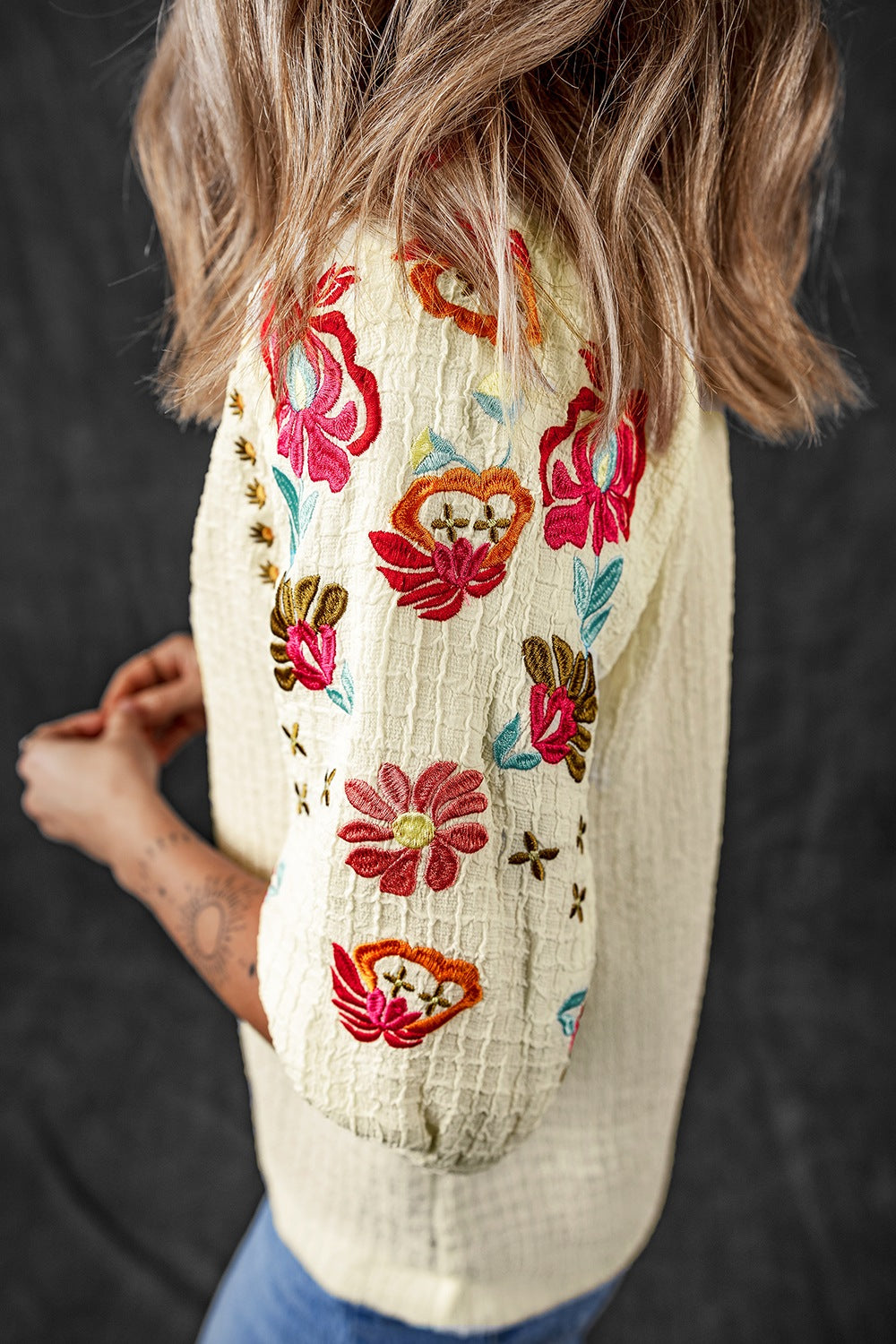 Beige blouse with voluminous embroidered sleeves featuring colorful floral and cross patterns.