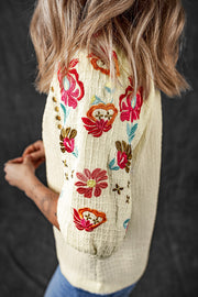 Beige blouse with voluminous embroidered sleeves featuring colorful floral and cross patterns.