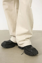 Oversized beige denim jeans with a sculpted leg, shown with black chunky sole shoes.