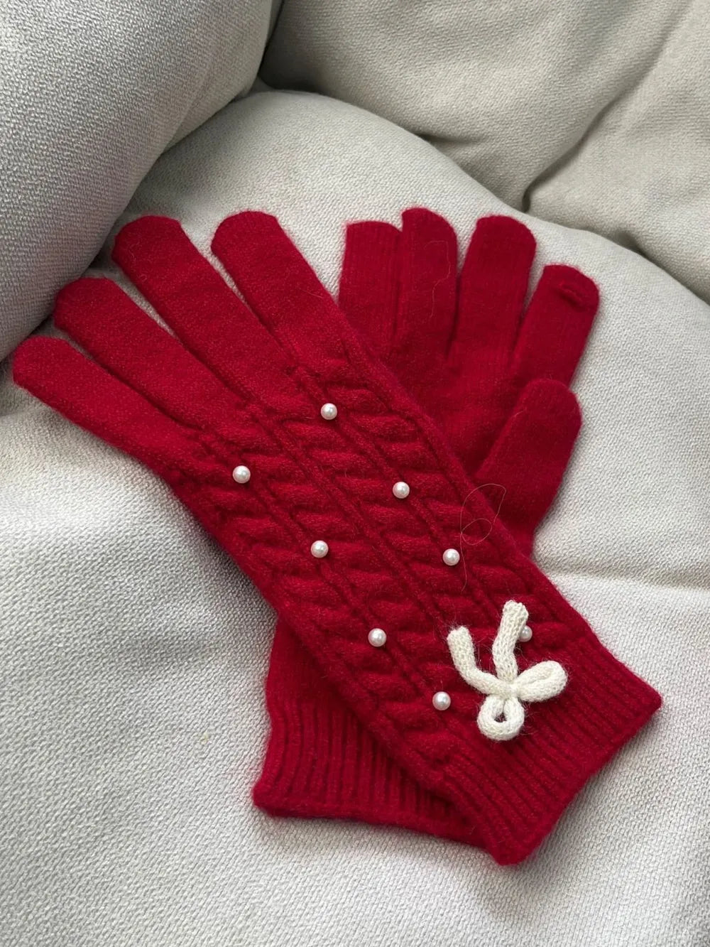 Red cable knit gloves with pearl embellishments and a white bow detail.