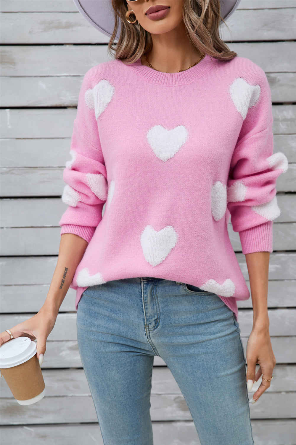 Pink crewneck sweater with white heart appliqués, long sleeves, casual acrylic knit.