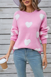 Pink crewneck sweater with white heart appliqués, long sleeves, casual acrylic knit.