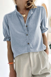 Light blue denim blouse with ruffled collar and puff sleeves, button front.