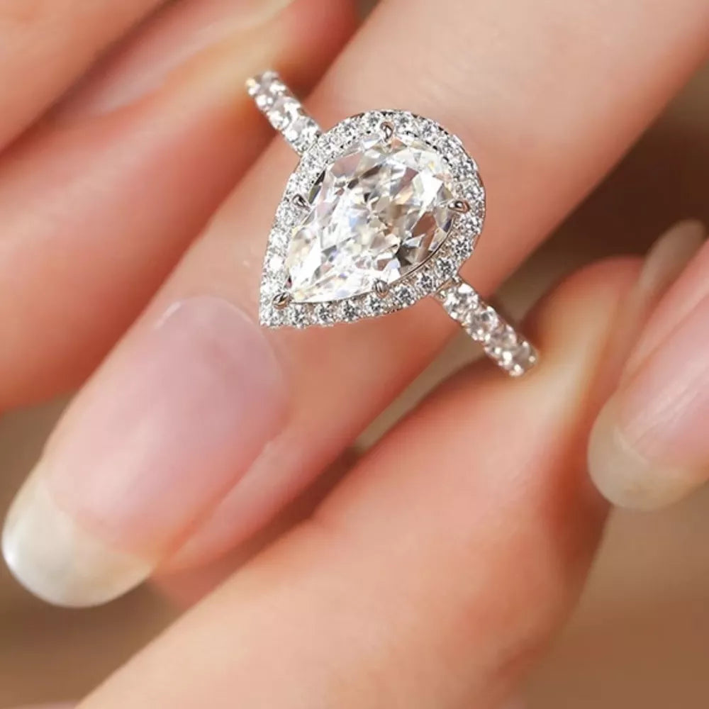 Elegant moissanite teardrop ring in sterling silver with halo setting and diamond band.