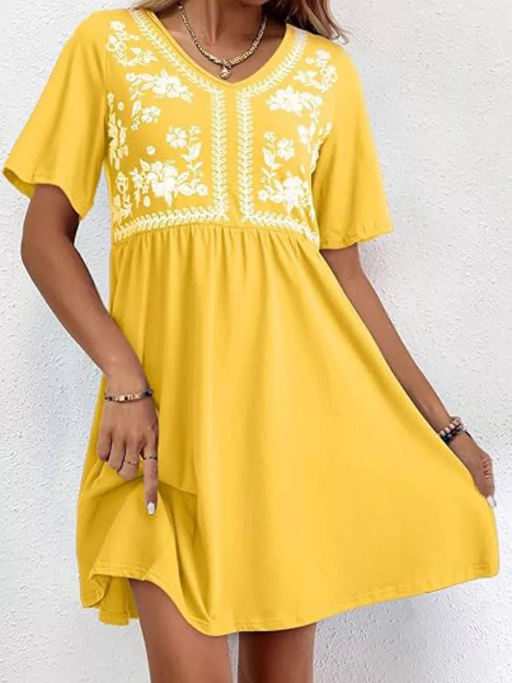 Yellow embroidered floral v-neck mini dress with short sleeves and a flowy skirt.