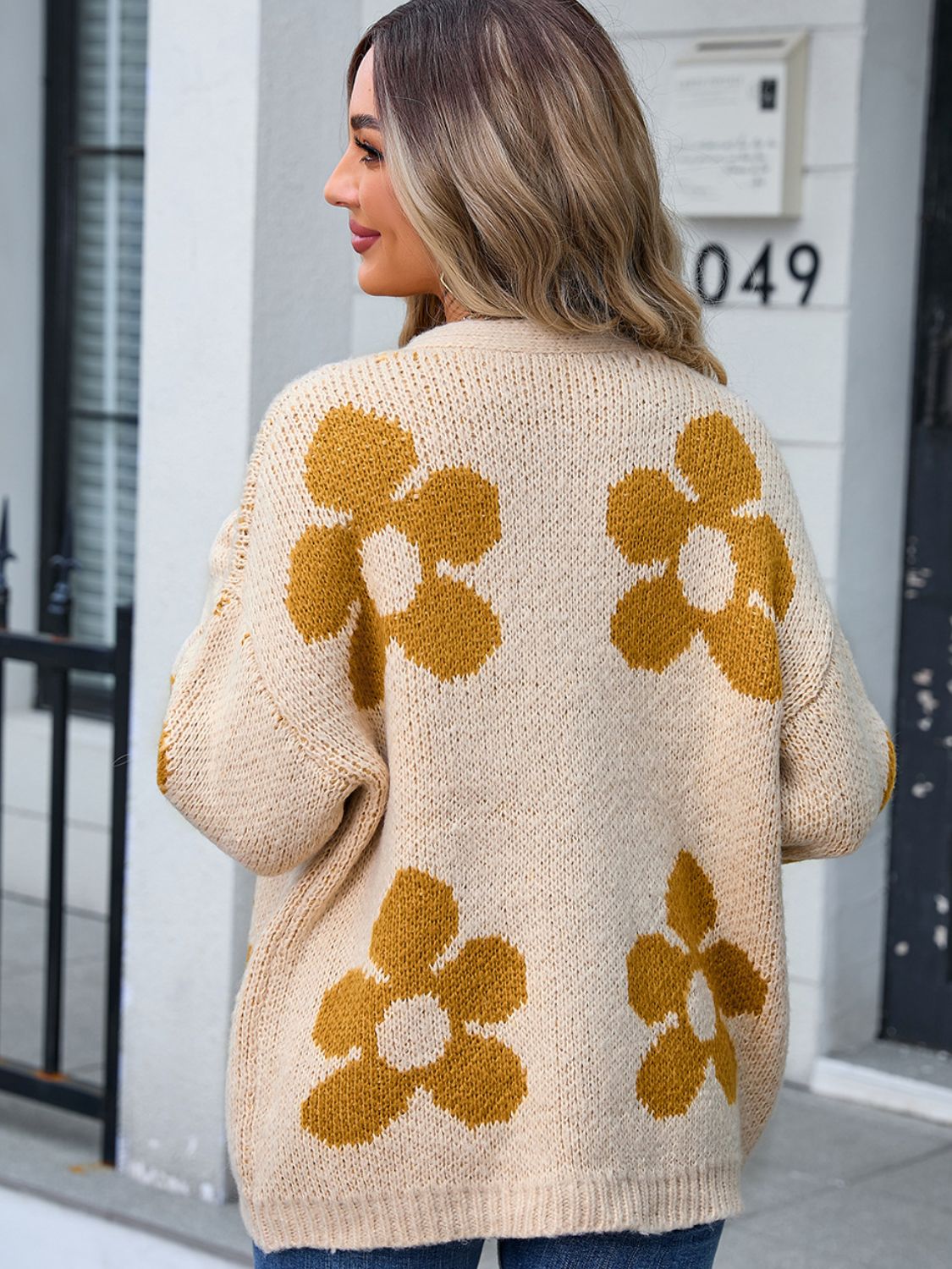 Tan knit cardigan with large mustard floral intarsia pattern, open front, long sleeves.