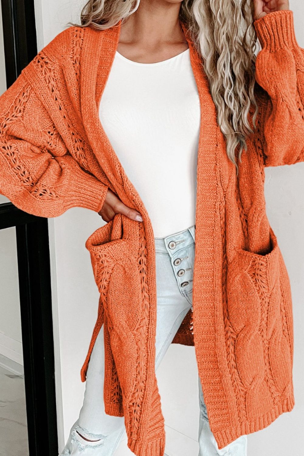 Burnt Coral cable knit open-front cardigan with pockets and intricate stitch details.