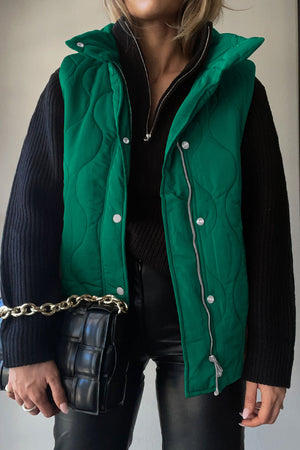 Green quilted stand-collar utility gilet with snap and zip front, worn over a black sweater.