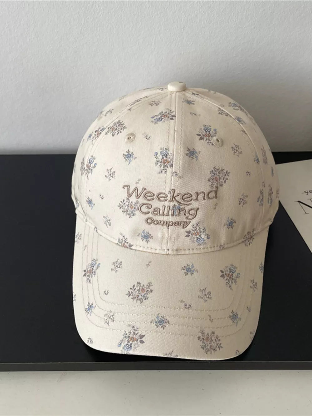Ivory floral embroidered baseball cap with "Weekend Calling Company" text.