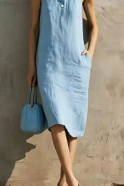 Light blue midi dress with button accents and pockets, sleeveless, crew neck, worn with a blue handbag.