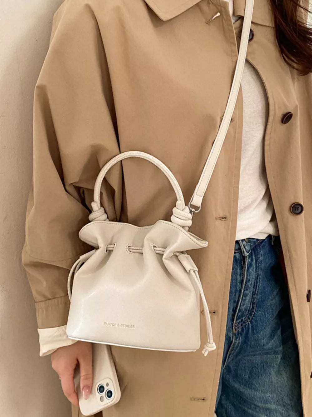 White pu leather cinch-top crossbody bag with knotted handle and drawstring closure.