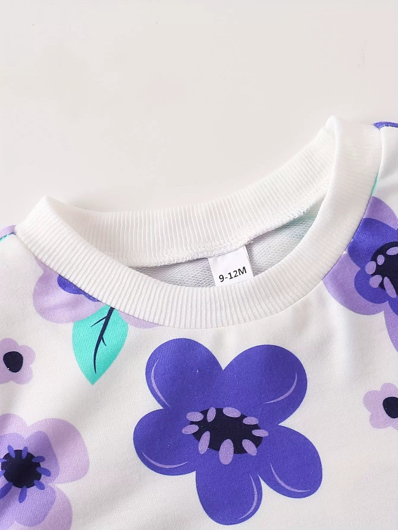 Baby crew neck top with purple and lavender floral print and ribbed collar.