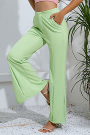 Neon green tailored trousers with split hems and pockets, styled with white sandals.
