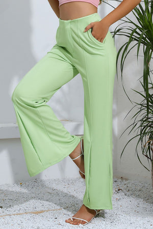 Neon green tailored trousers with split hems and pockets, styled with white sandals.