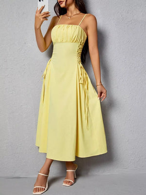 Light yellow cami dress with ruched bodice and crisscross lace-up sides, A-line skirt.