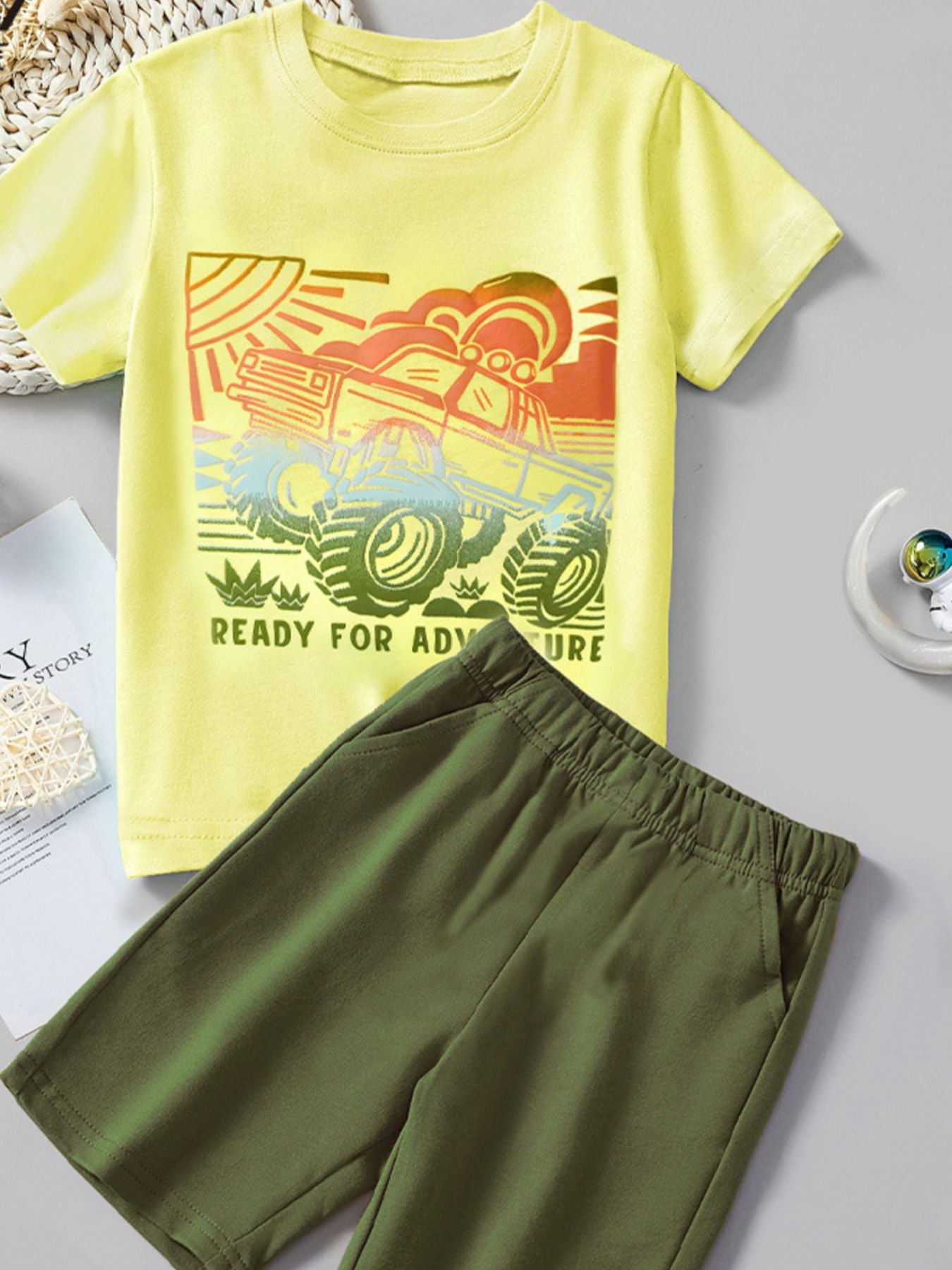 Yellow cotton t-shirt with monster truck graphic and green shorts.
