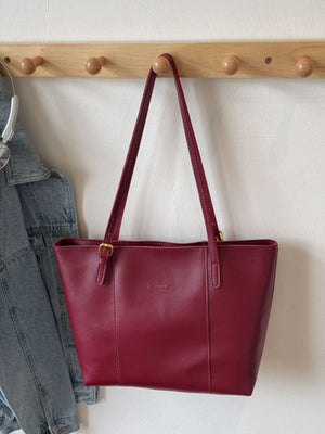 Wine red structured PU leather tote bag with gold buckle detail and embossed logo.