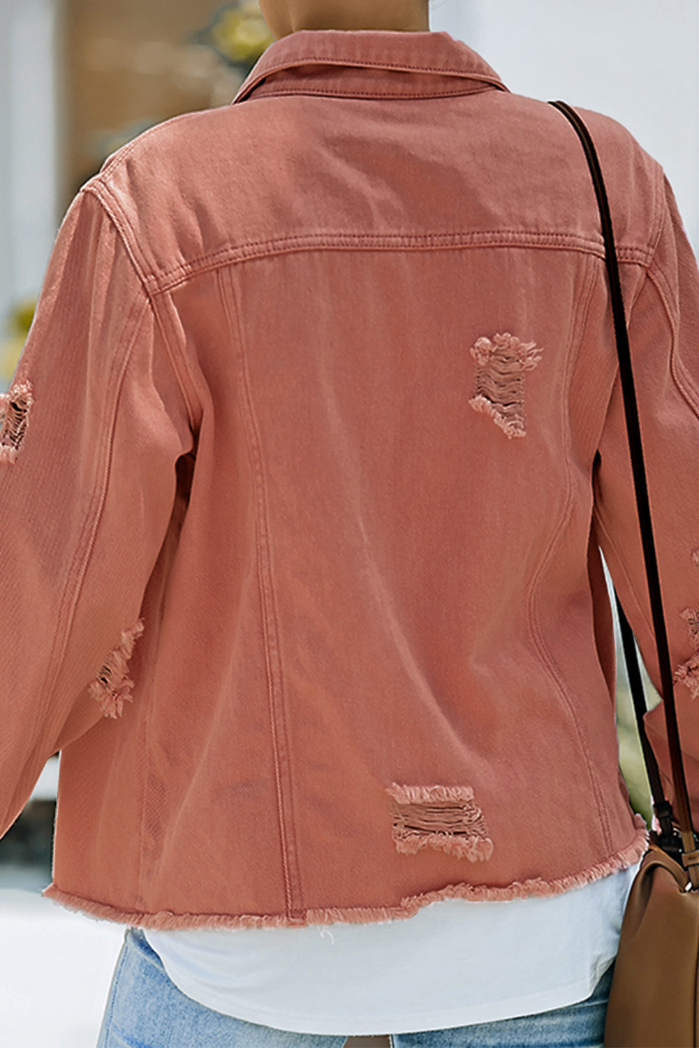 Distressed denim trucker jacket in salmon with frayed edges and rips.