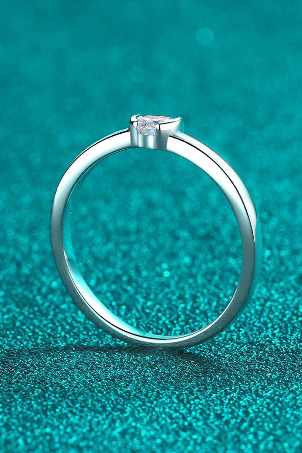 Silver ring with a heart-cut solitaire diamond on a textured teal background.
