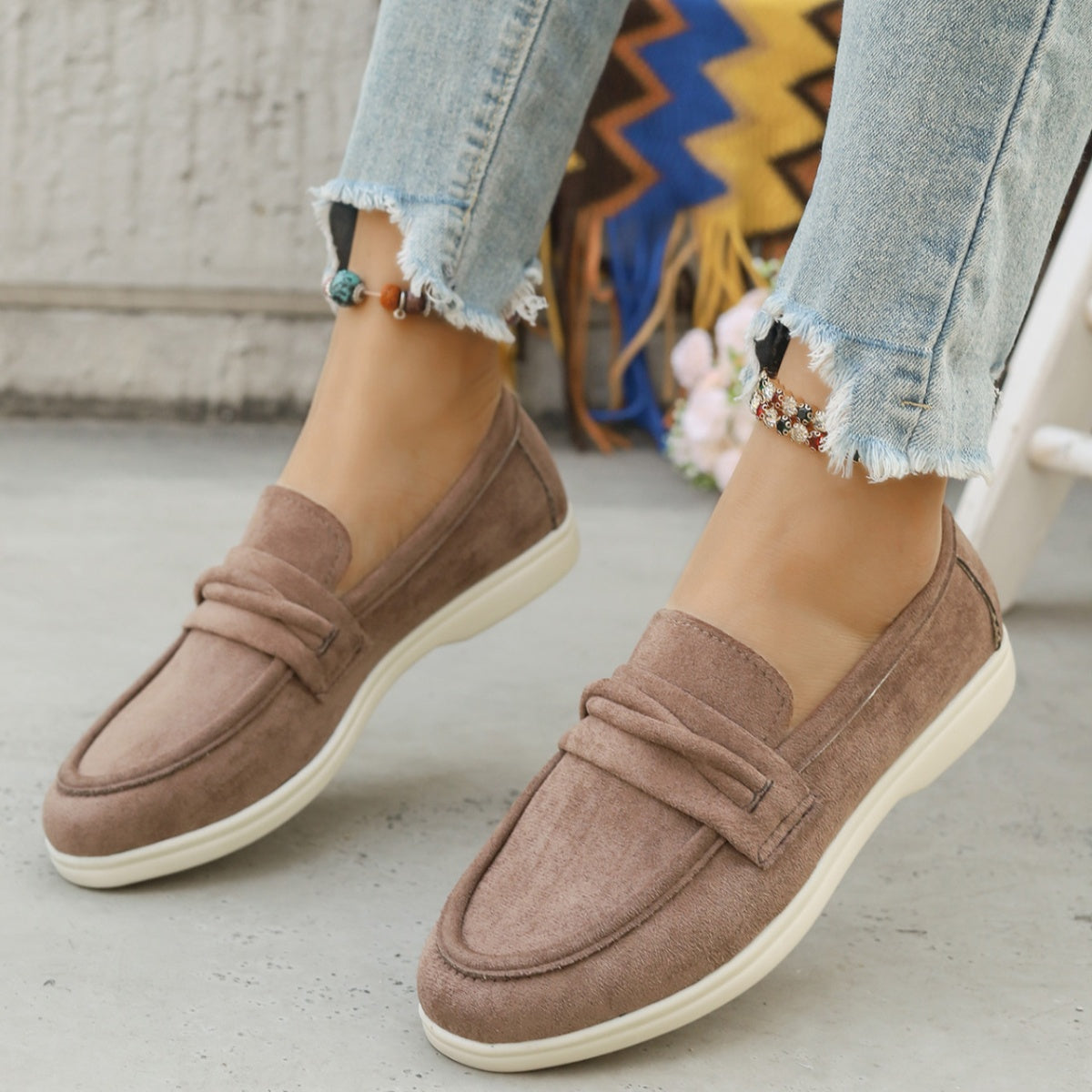 Beige round toe slip-on loafers with ruched strap detail and white soles.