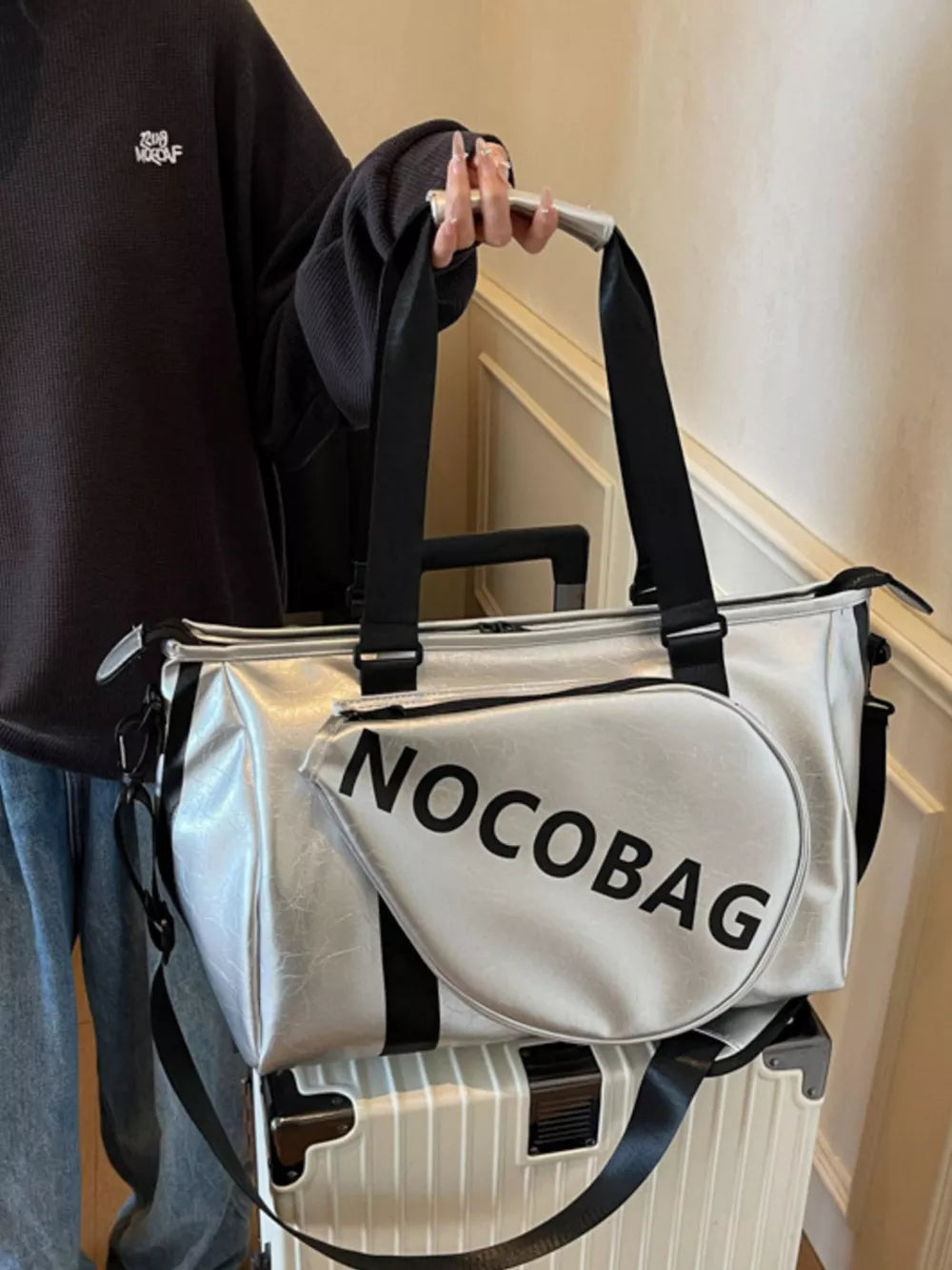 Silver leather duffel bag with black trim and "NOCOBAG" text, detachable strap.