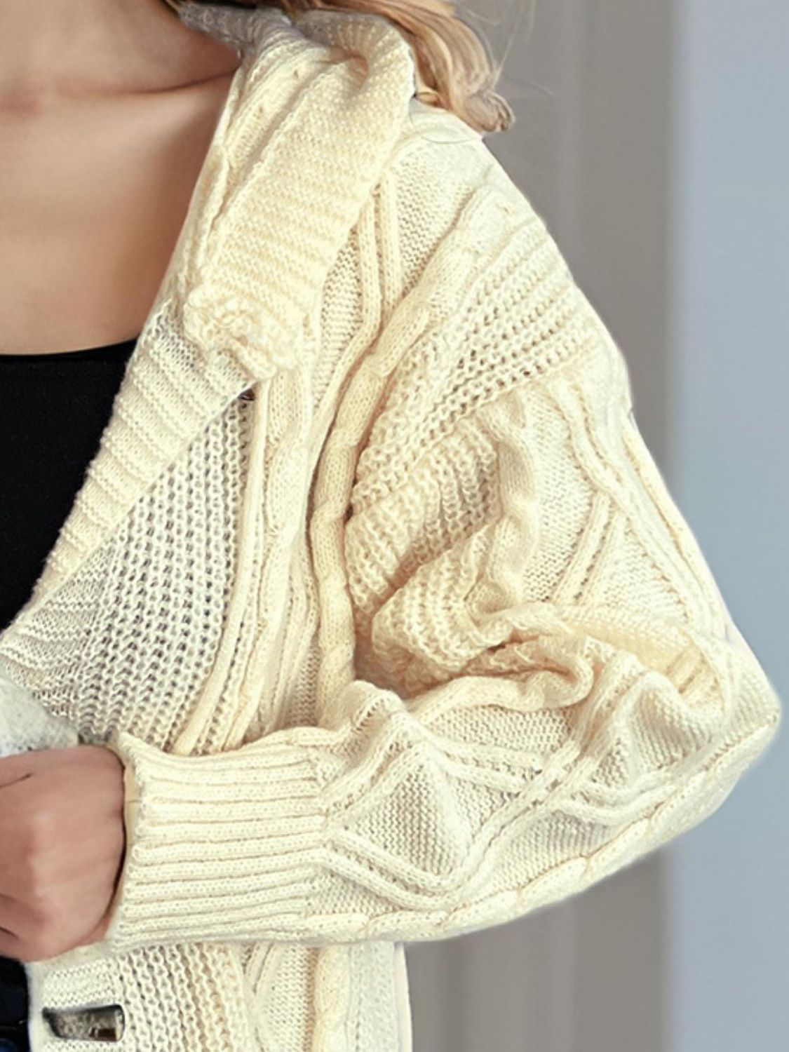 Beige cable knit hoodie with toggle closure and textured sleeves.