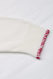 White knit sweater sleeve with red contrast stitching detail