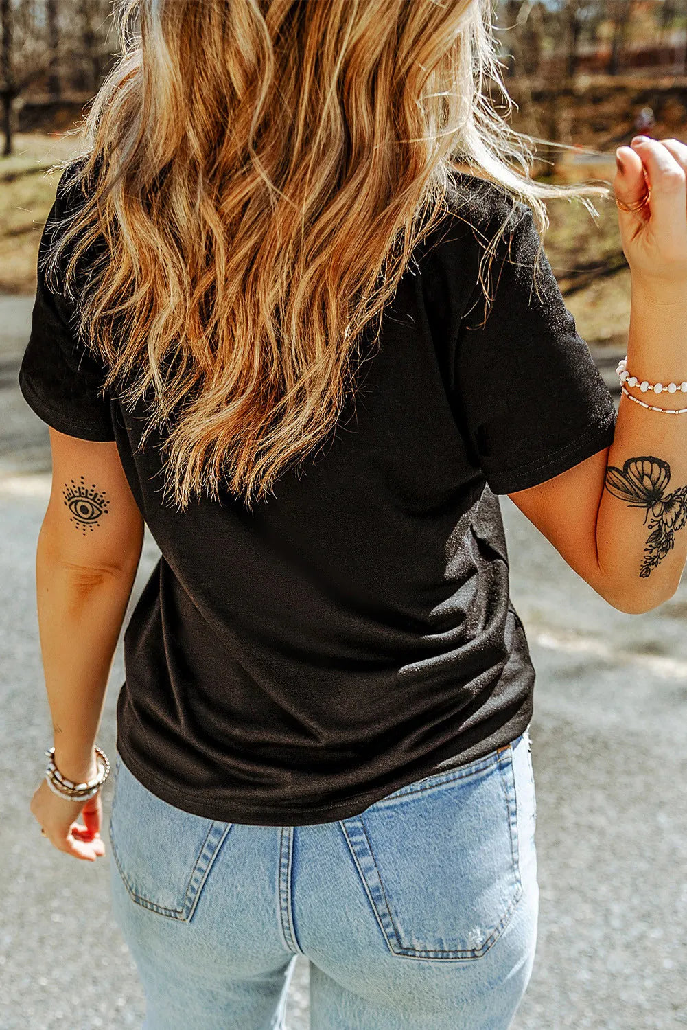 Black graphic tee with short sleeves and a retro font design, paired with light wash jeans.