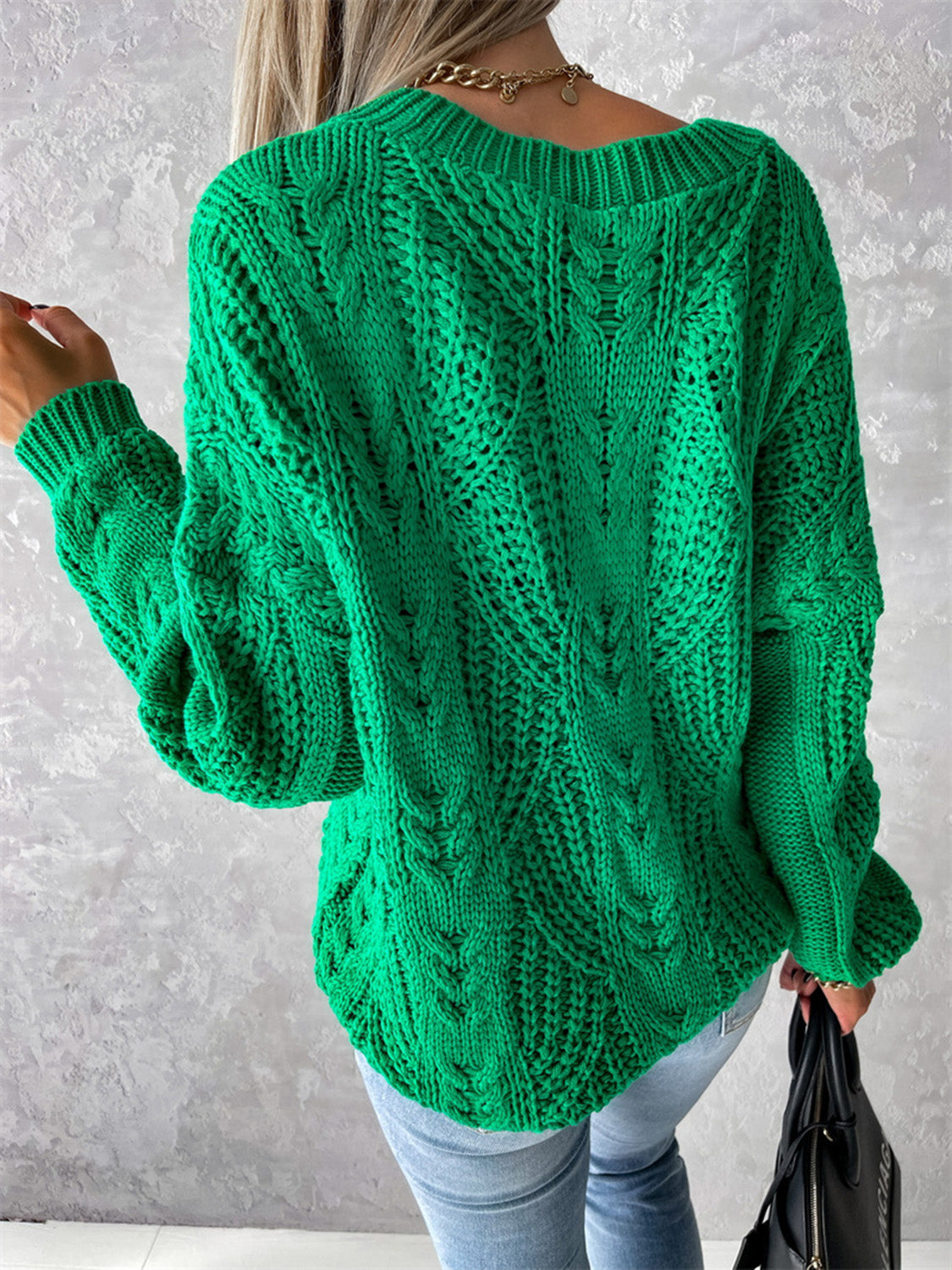 Green cable knit sweater with V-neck and relaxed fit, featuring intricate stitching details.