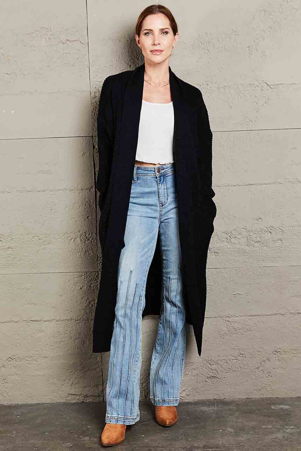 Black textured knit maxi cardigan with open front and pockets, styled with a white crop top and flared jeans.