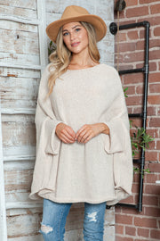 Cream knit sweater with cape sleeves and a relaxed fit, styled with jeans and a hat.