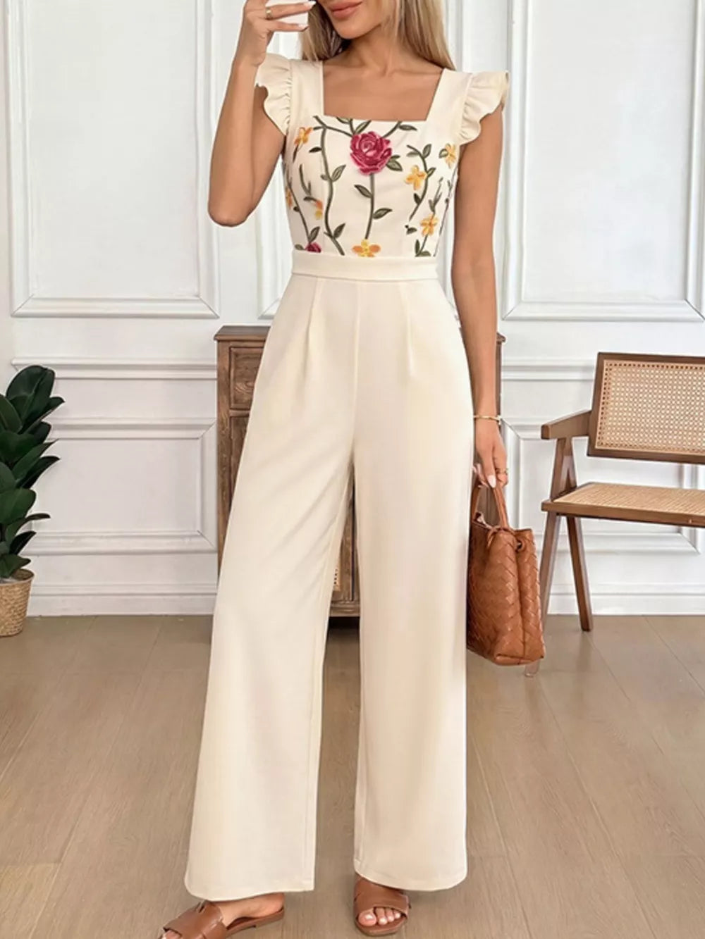 Beige floral embroidered ruffle jumpsuit with square neckline and wide legs.